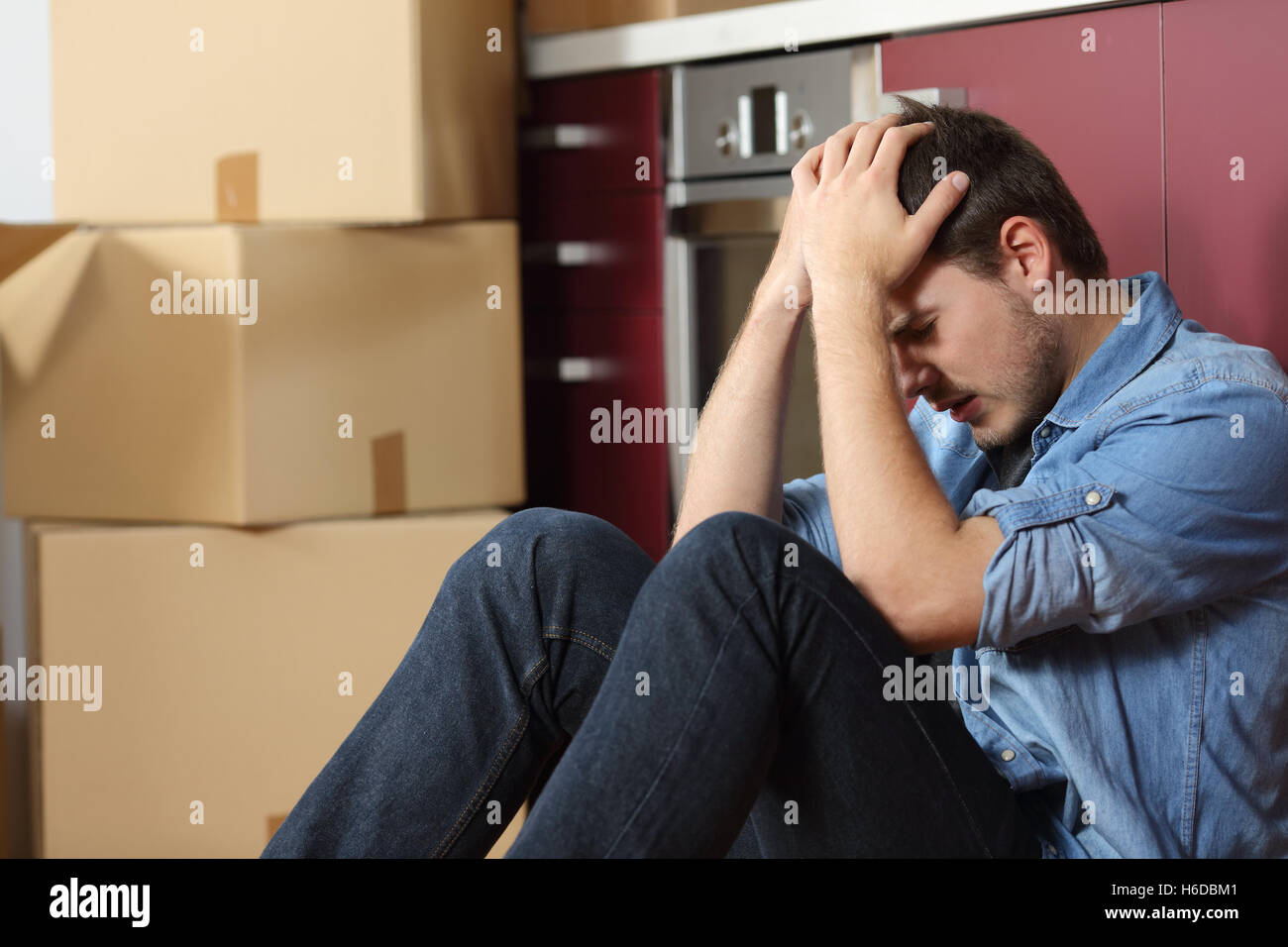 Triste sfrattati uomo preoccupato il riposizionamento casa seduto sul pavimento in cucina Foto Stock