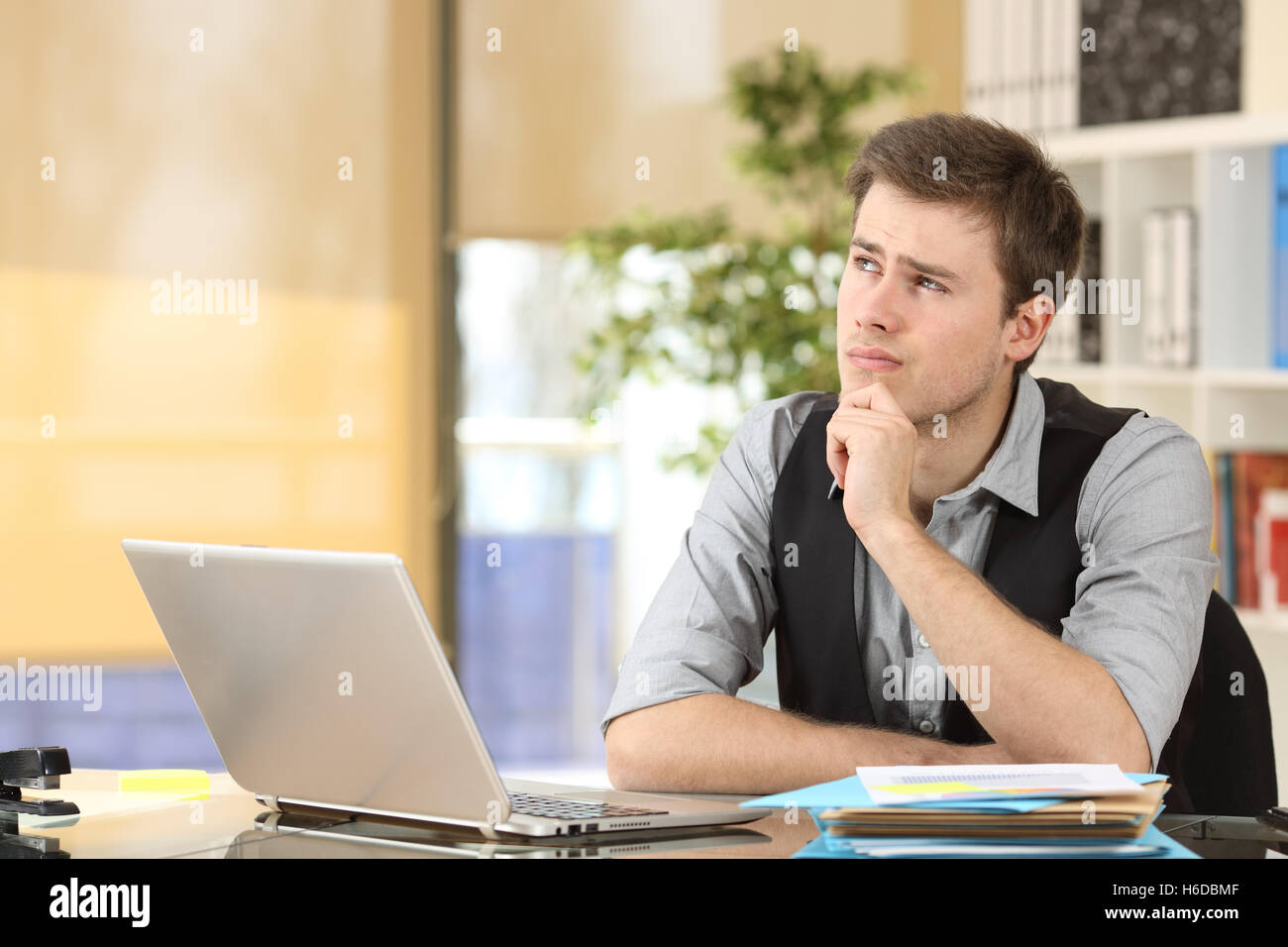 Serio dubbio imprenditore pensando e guardando dal lato seduta a una scrivania in ufficio Foto Stock