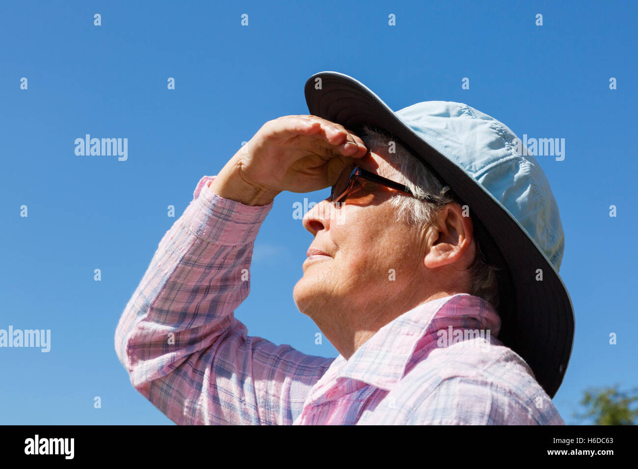 Un senior donna che indossa una vasta colmato cappello e occhiali scuri in sfumature di sole gli occhi per guardare lontano fino al sole in estate. Inghilterra Regno Unito Gran Bretagna Foto Stock