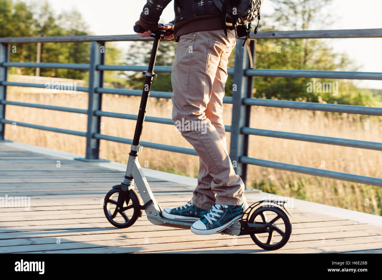 Giovane uomo in abbigliamento casual su kick scooter in parco al tramonto Foto Stock