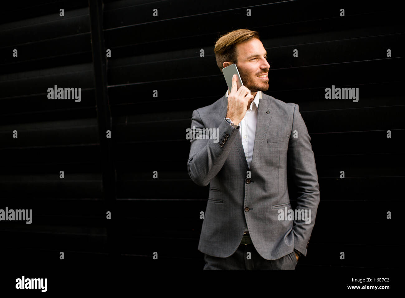 Imprenditore con un telefono dal muro nero Foto Stock