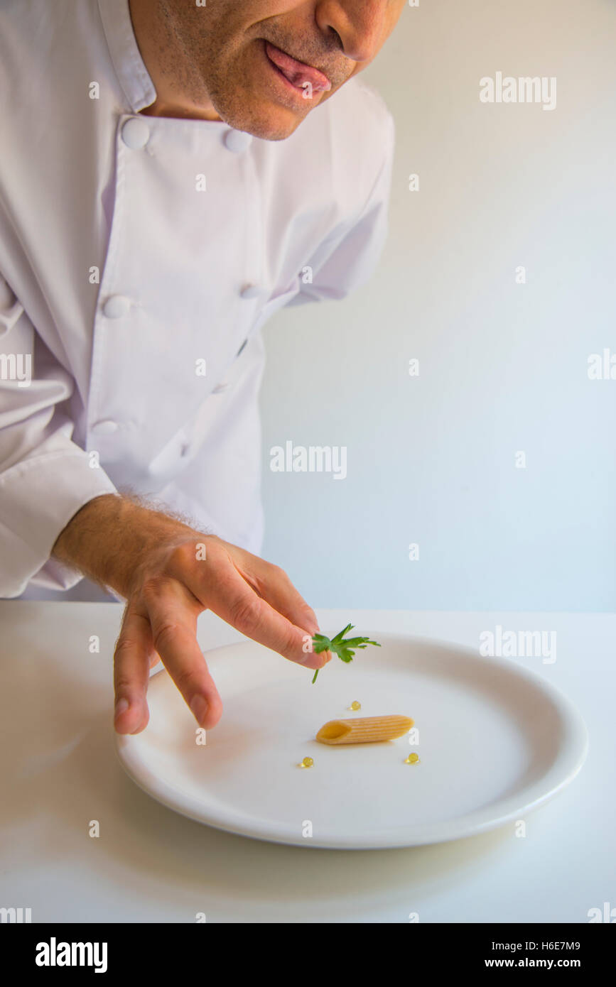 La nouvelle cuisine: minimalismo. Umoristico. Lo Chef mettendo una foglia di prezzemolo sulla parte superiore di un singolo maccheroni. Foto Stock