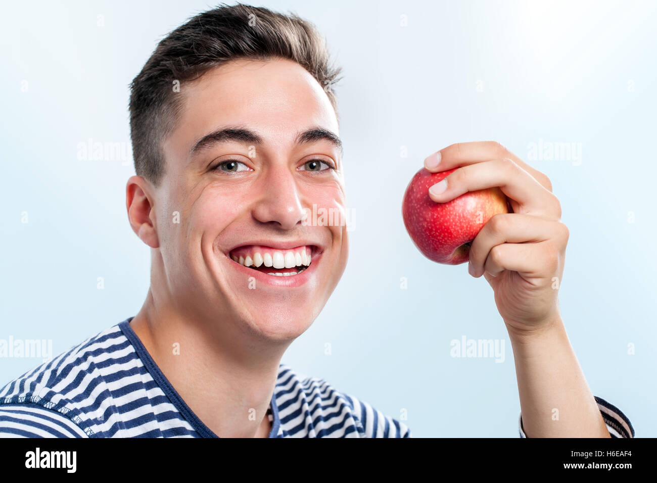 Extreme close up del bel giovane adolescente azienda red apple e mostrando i denti sani. Foto Stock
