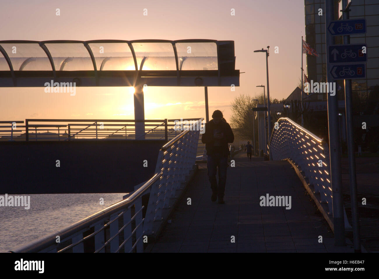 Sunset silhouette dell uomo a camminare con il ciclista in background sul lato del fiume passerella Foto Stock
