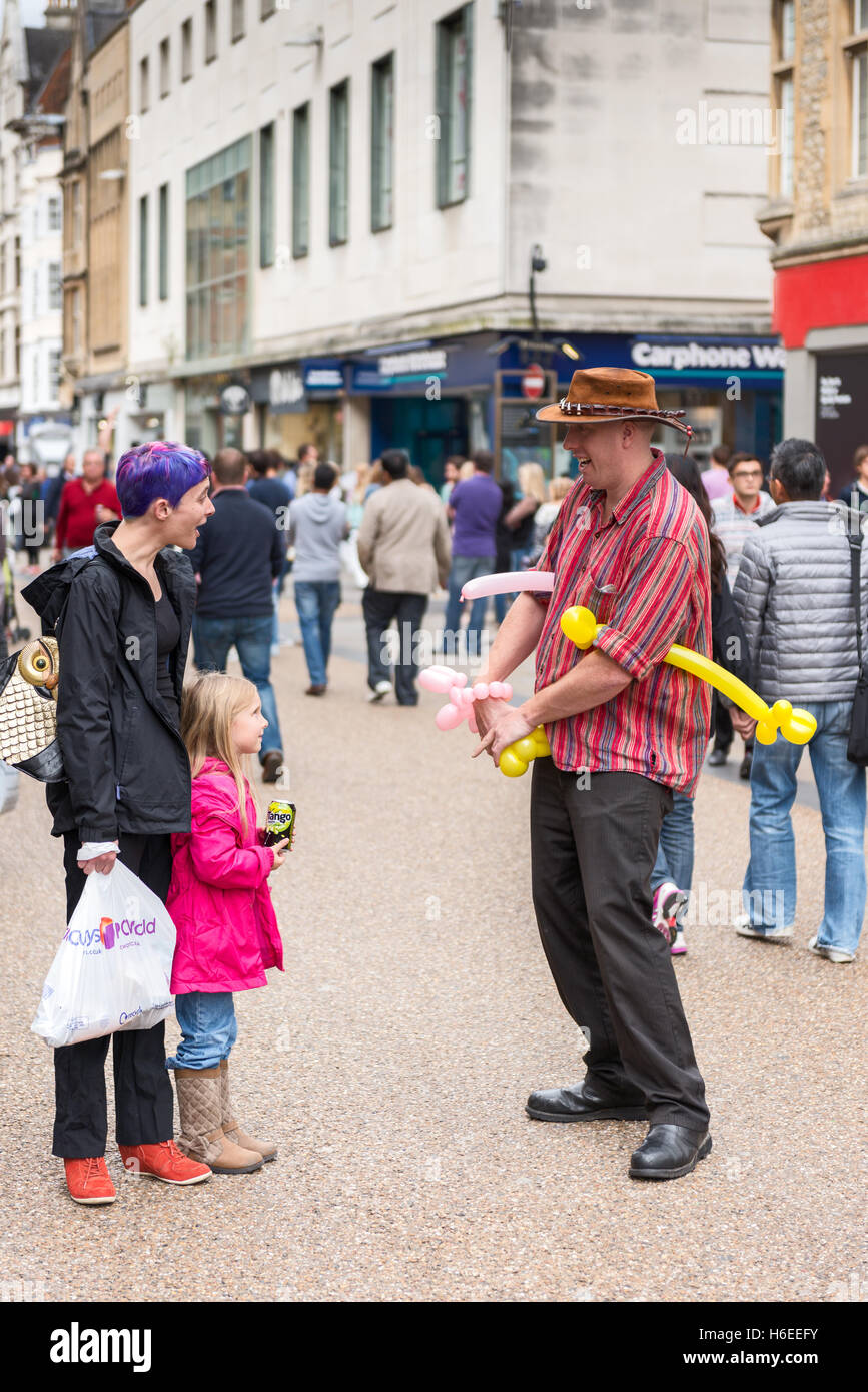 L'artista di strada intrattiene la bambina e la mamma con palloncini su Cornmarket Street, Oxford, UK Foto Stock
