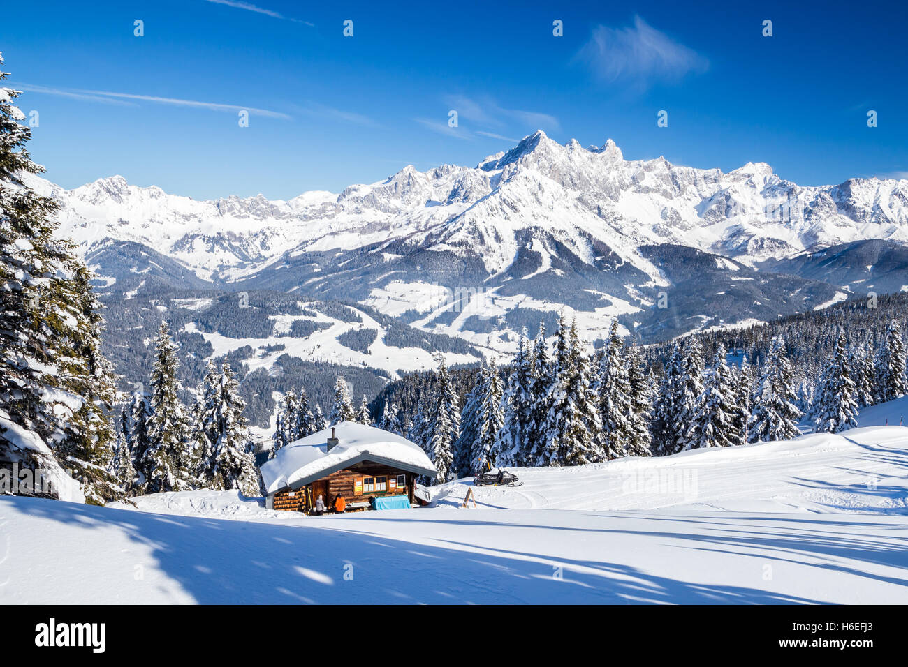 Log Cabin in un paesaggio di montagna nel mezzo dell'inverno in una giornata di sole con vista sulle imponenti montagne. Foto Stock