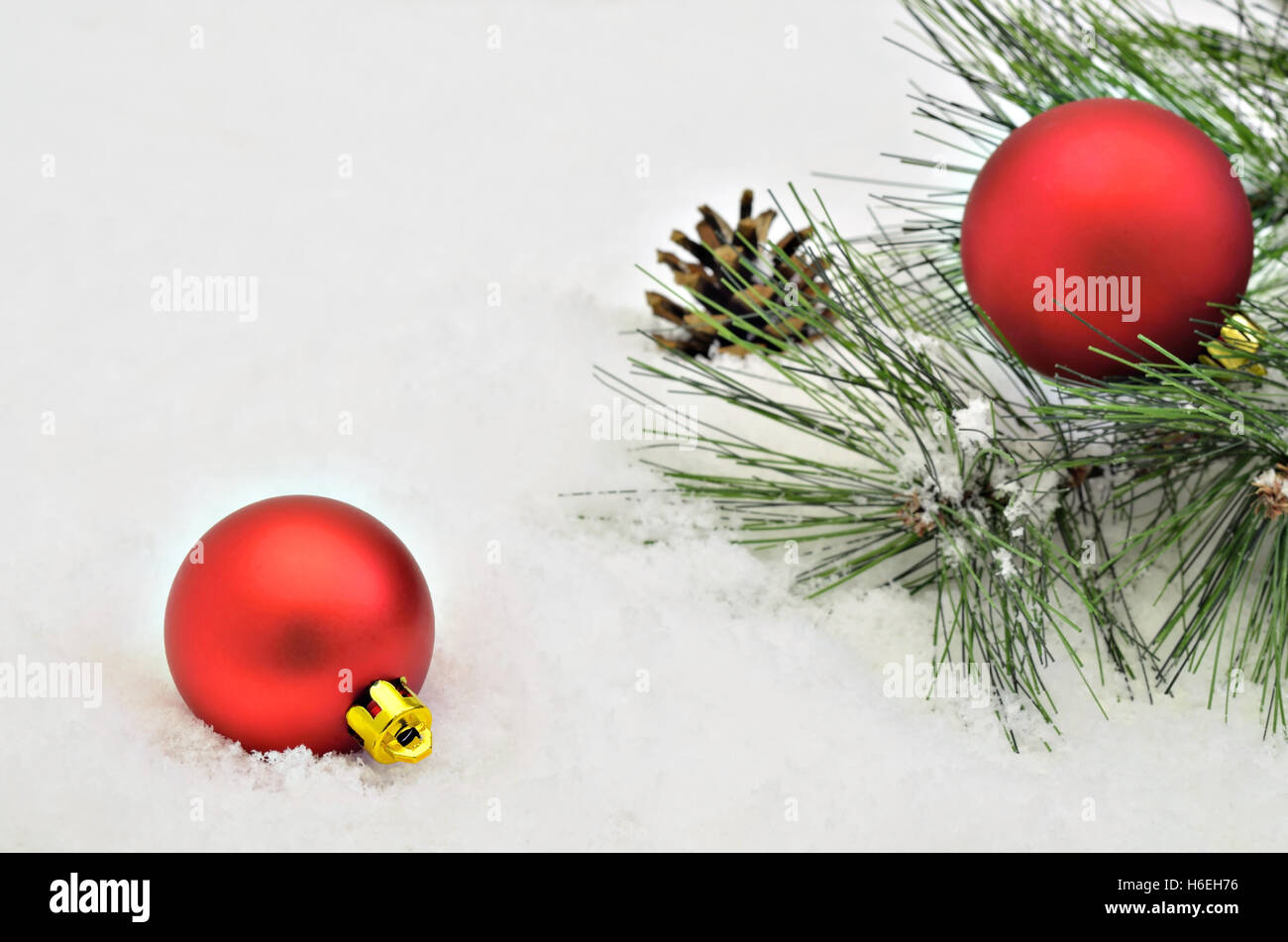 Due red albero di Natale le sfere con rametti di abete e pino cono su sfondo di neve, macro close up, spazio per testo, orizzontale Foto Stock