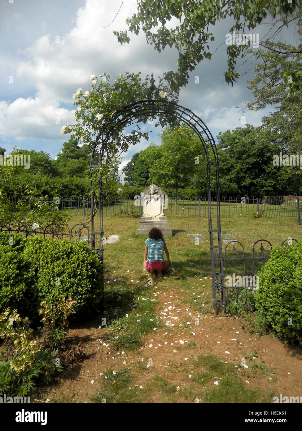 Ragazza in ginocchio davanti a un monumento nel cimitero Foto Stock