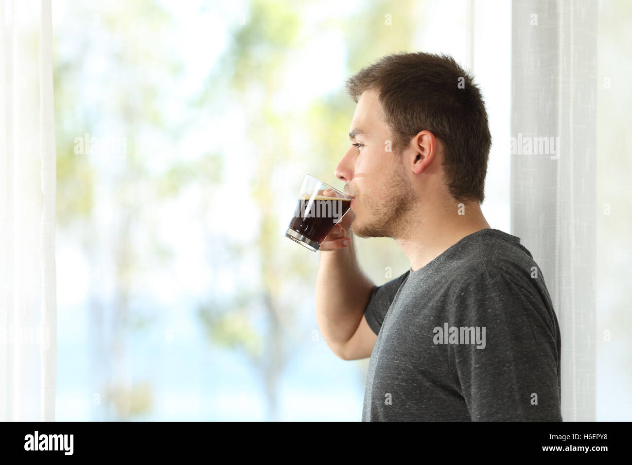 Vista laterale di un uomo di bere il caffè guardando attraverso la finestra di casa o hotel Foto Stock