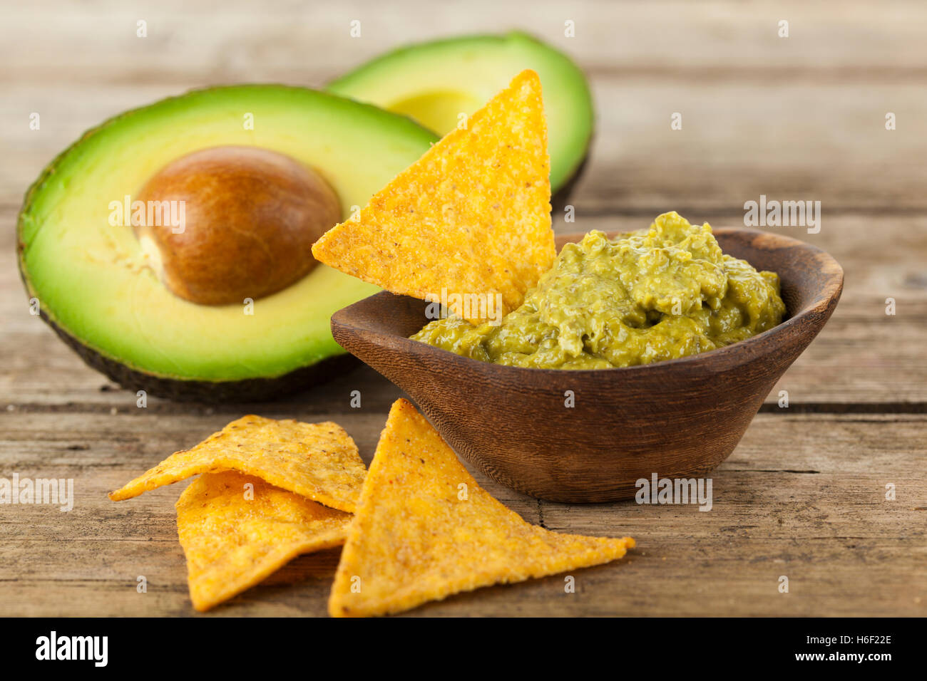 Ciotola di legno riempita con salsa guacamole, nachos e dimezzato avocado sul tavolo rustico Foto Stock