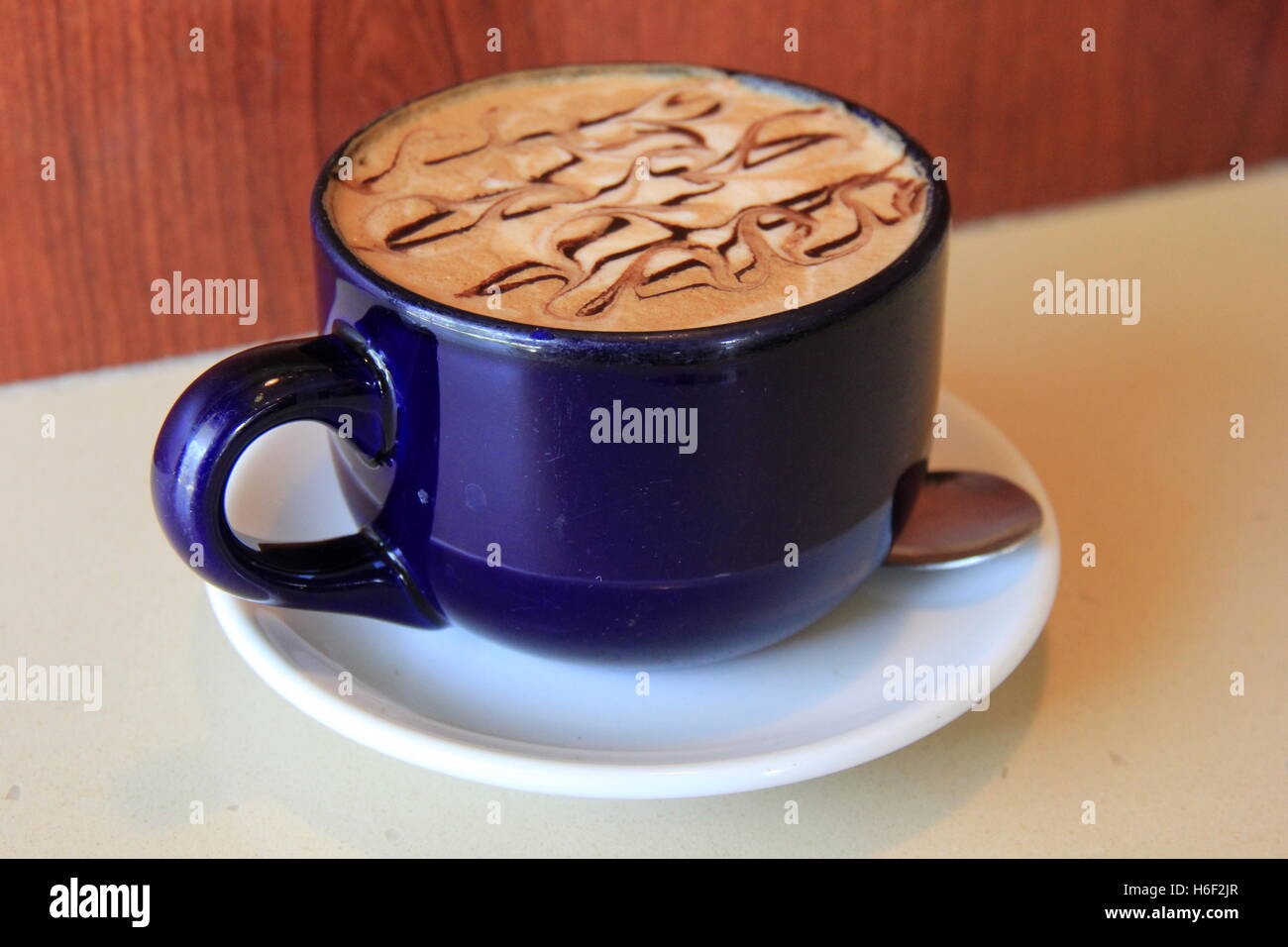 La tentazione di tazza di cappuccino Moka spruzzata con scuri di sciroppo al cioccolato in tazza blu. Foto Stock