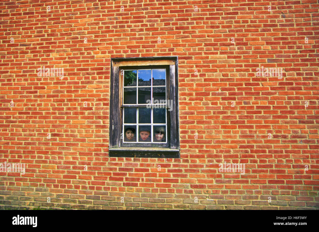 Tre bambini in una finestra in su una vecchia casa in mattoni rossi. Foto Stock