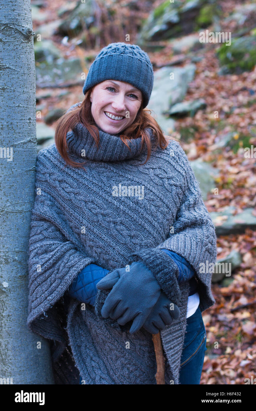 Una donna glamour escursioni attraverso i boschi in autunno caduta stagione indossando un informale poncho di lana di abbigliamento per il tempo libero cappellino guanti Foto Stock