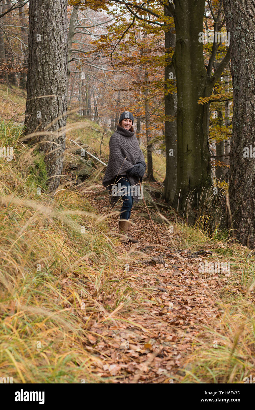 Una donna glamour escursioni attraverso i boschi in autunno caduta stagione indossando un informale poncho di lana di abbigliamento per il tempo libero cappellino o a piedi Foto Stock