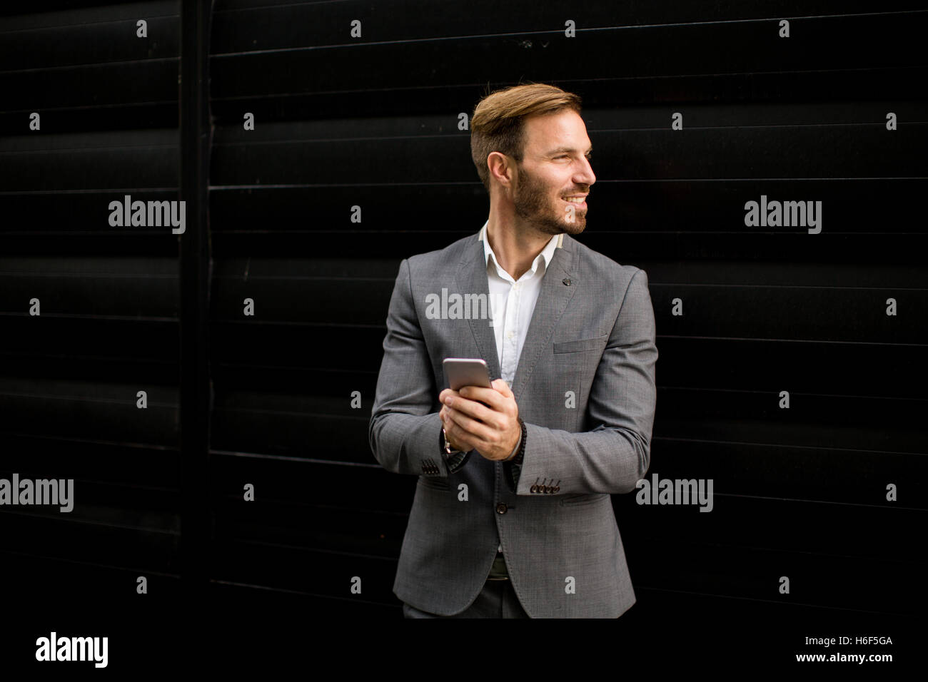 Imprenditore con un telefono dal muro nero Foto Stock
