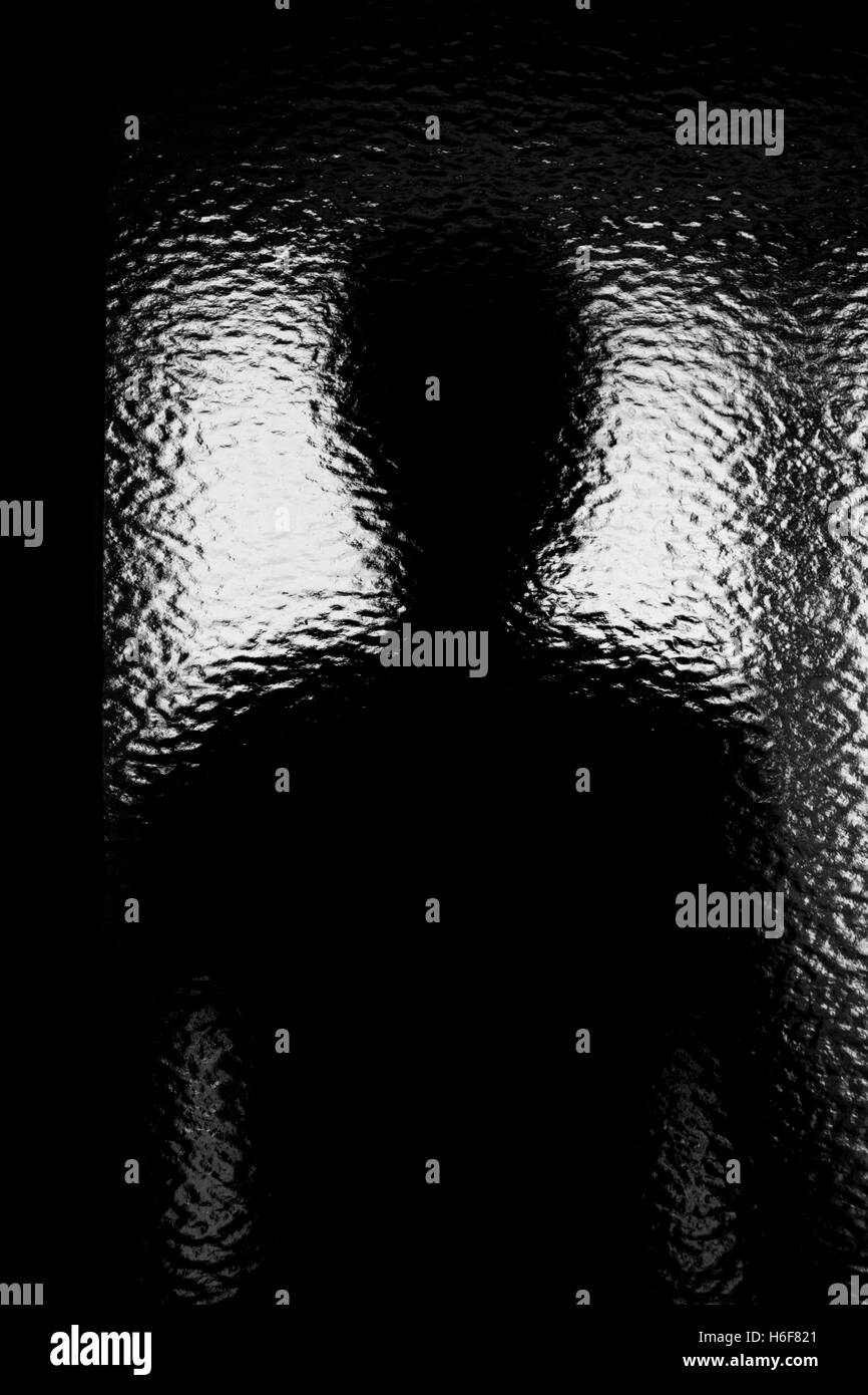 Silhouette di una persona anonima attraverso accidentato il vetro. Monocromatico Foto Stock