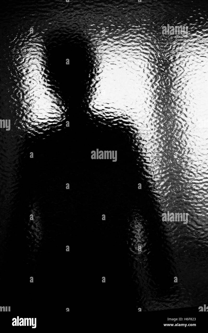 Silhouette di una persona anonima attraverso accidentato il vetro. Monocromatico Foto Stock
