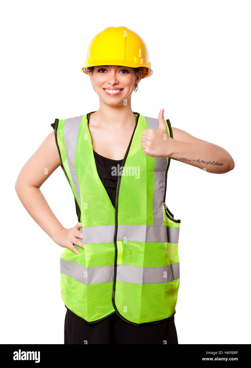 Giovani caucasici donna adulta nei suoi metà di 20s indossando riflettivo giallo casco di sicurezza e giubbotto di sicurezza" dando la telecamera il pollice Foto Stock