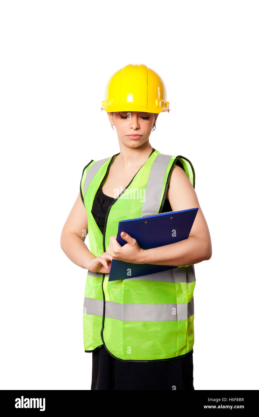 Giovani caucasici donna adulta nei suoi metà di 20s indossando riflettivo giallo casco di sicurezza e giubbotto di sicurezza, guardando verso il basso in corrispondenza di una clipboard Foto Stock