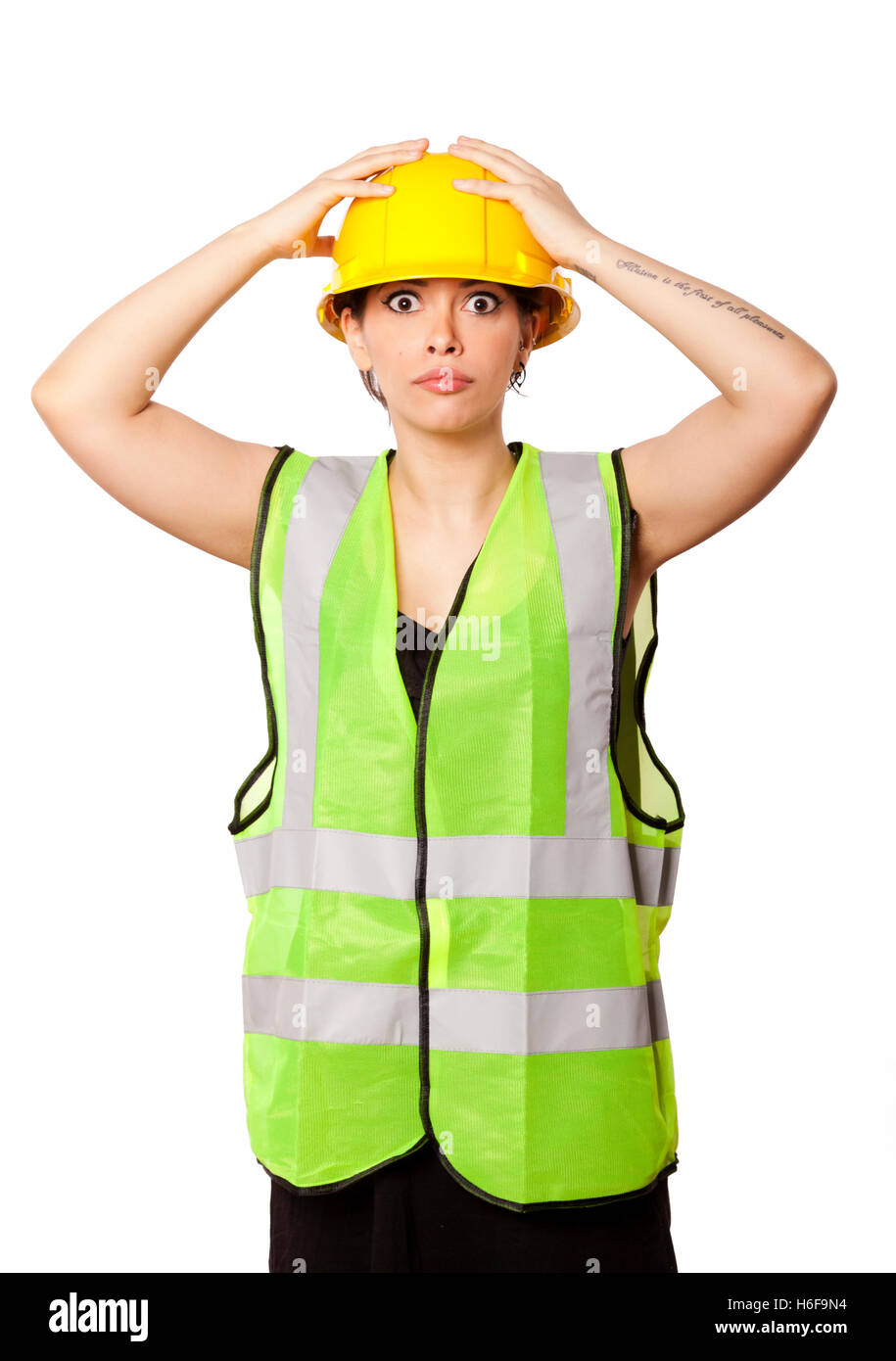 Giovani caucasici donna adulta nei suoi metà di 20s indossando riflettivo giallo casco di sicurezza e giubbotto di sicurezza, alzando le mani sul suo hat Foto Stock