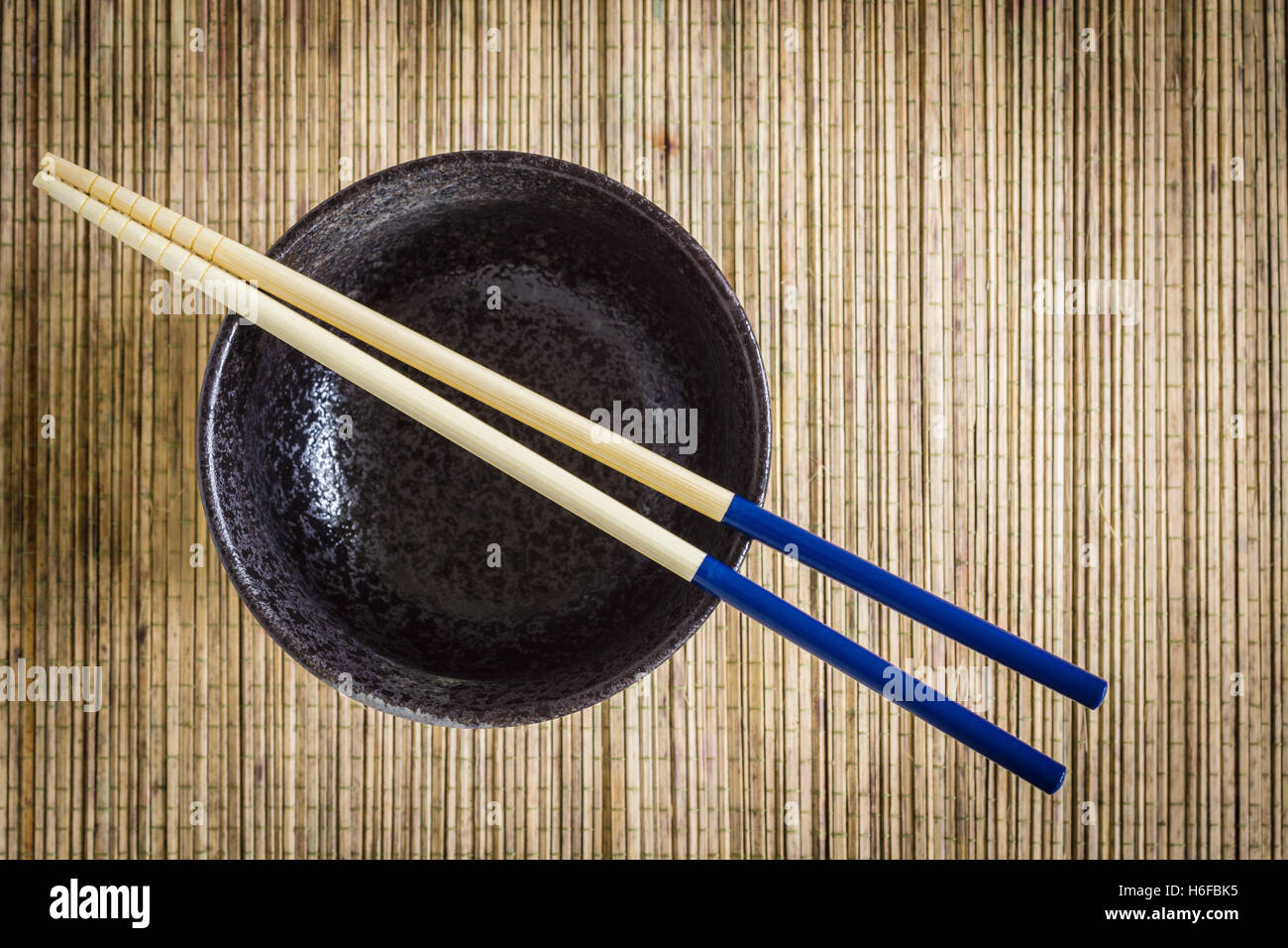 Bacchette e Riso o Noodle bowl contro un tappetino di bambù lo sfondo ideale per piatti Asiatici soggetti Foto Stock