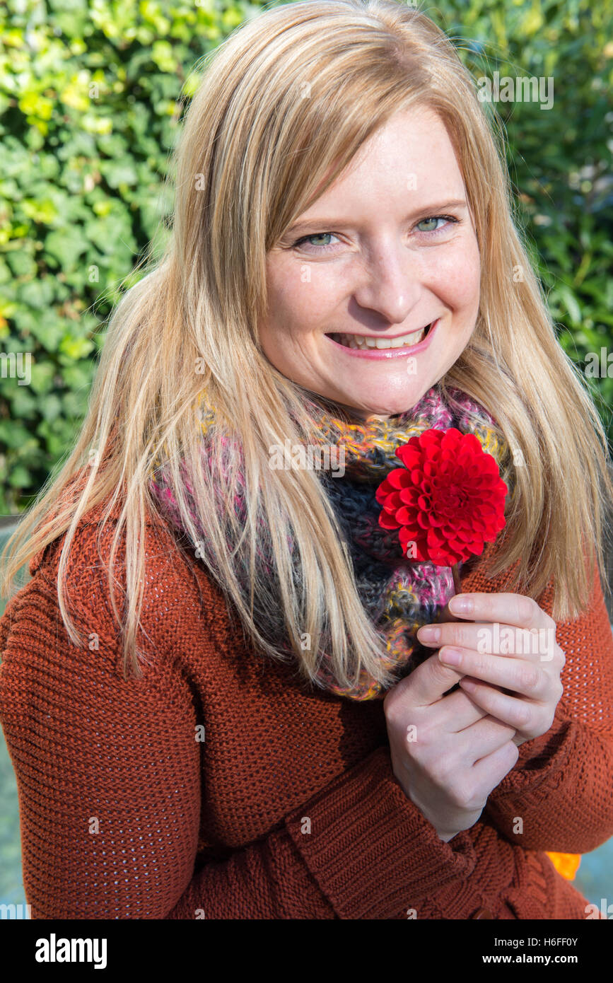 Donna attraente con il fiore in mano per godersi il sole in autunno Foto Stock