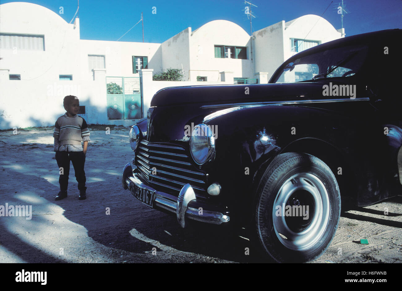 La Tunisia, Jarbah Isola, ragazzo di fronte a un vecchio Peugeot 203 di Houmt Souk. Foto Stock