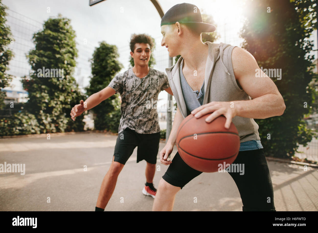 Due giovani amici giocare a basket sulla corte all'aperto e divertirsi. Streetball giocatori avente un gioco di pallacanestro. Foto Stock