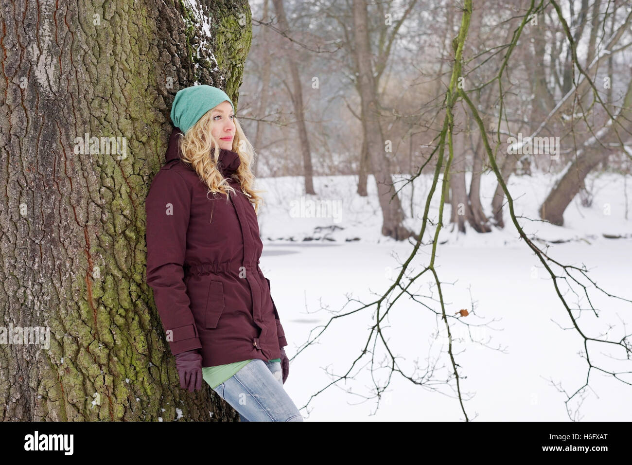 Malinconici donna appoggiata ad albero in inverno Foto Stock