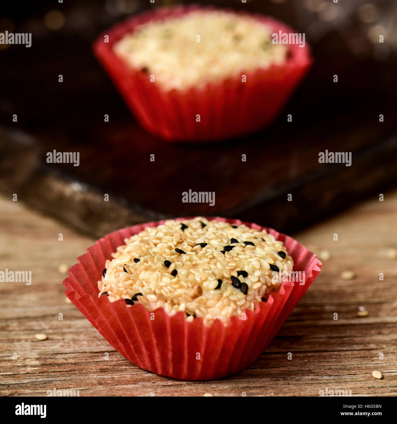 Dettaglio di alcuni di sesamo giapponese mochi dolci in carta rossa casi su una tavola in legno rustico Foto Stock
