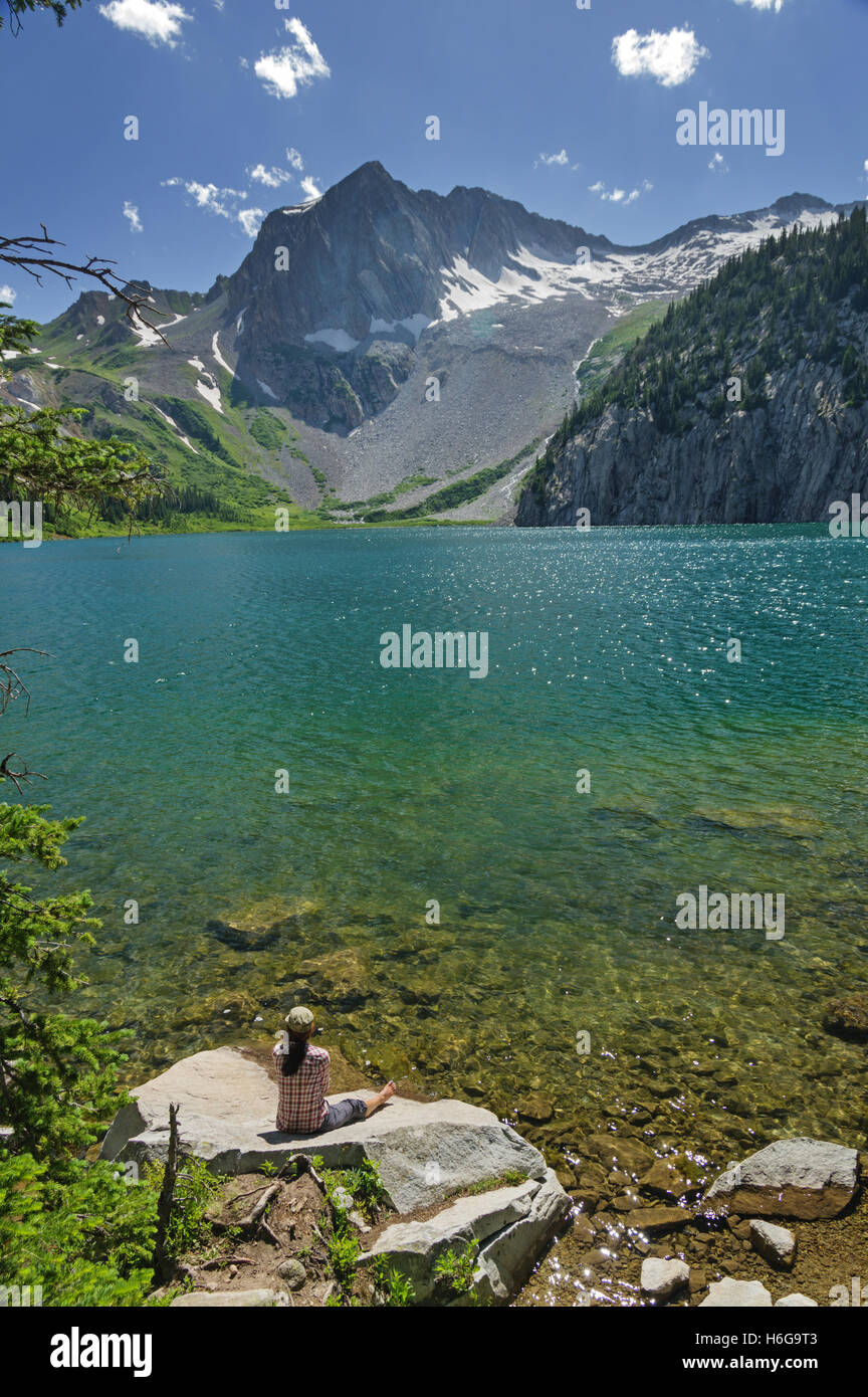 La donna si siede su una roccia sulla riva del lago Snowmass in Colorado Foto Stock