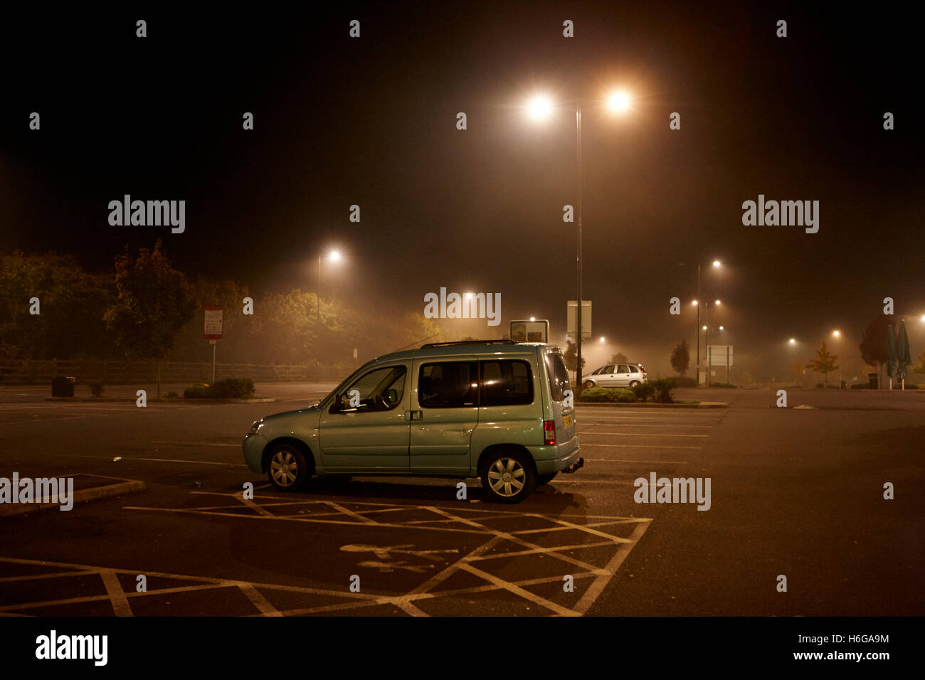 Auto parcheggiate durante la notte nel parcheggio di una stazione di servizio autostradale nella nebbia England Regno Unito Foto Stock