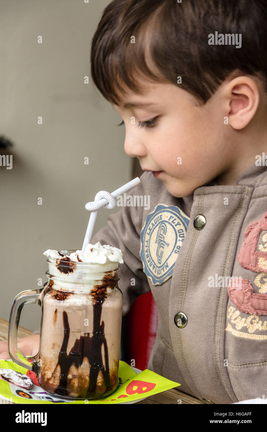 Un giovane ragazzo di bere una tazza di cioccolata calda la torta con panna montata. Foto Stock