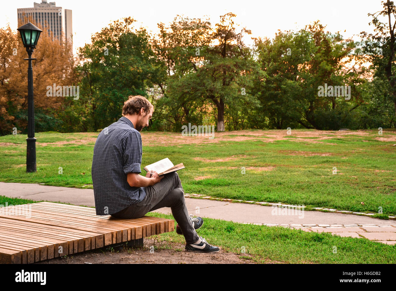 Ragazzo seduto su una panchina nel parco libro di lettura Foto Stock