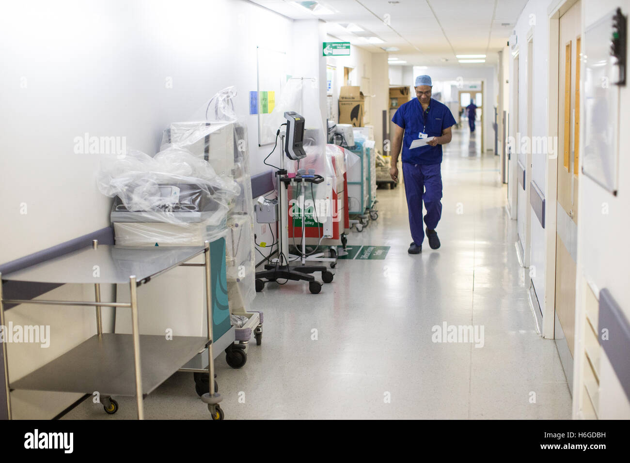 Un chirurgo passeggiate lungo un NHS hospital corridoio indossando scrubs Foto Stock