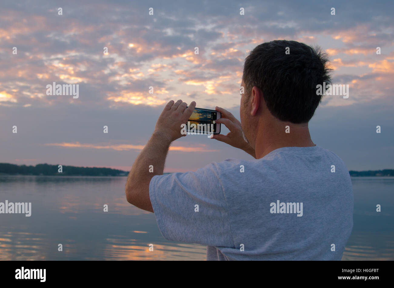 Uomo in un lago di fotografare alba con smart phone Foto Stock