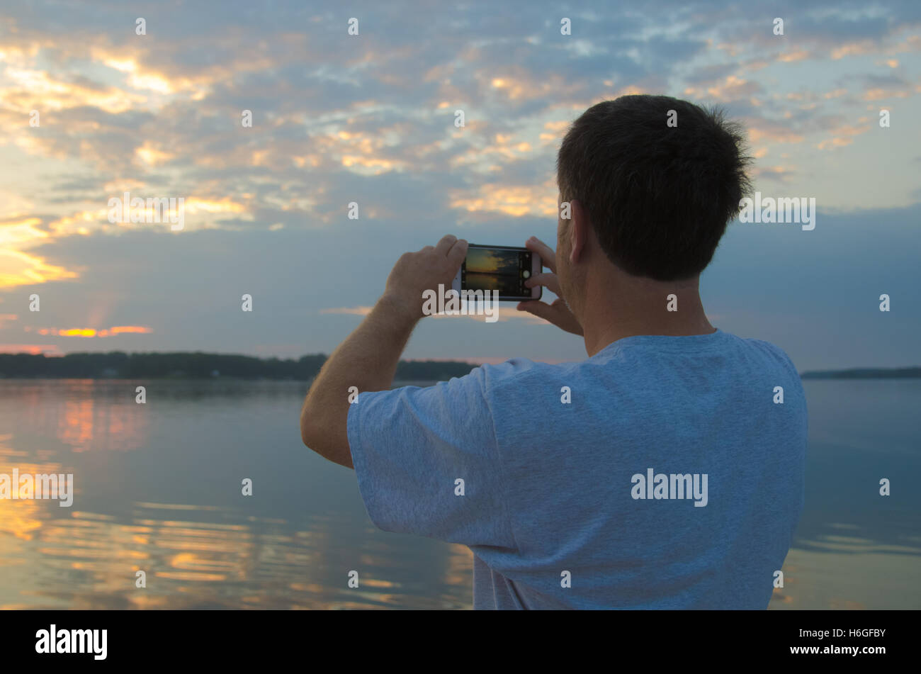 Uomo in un lago di fotografare alba con smart phone Foto Stock