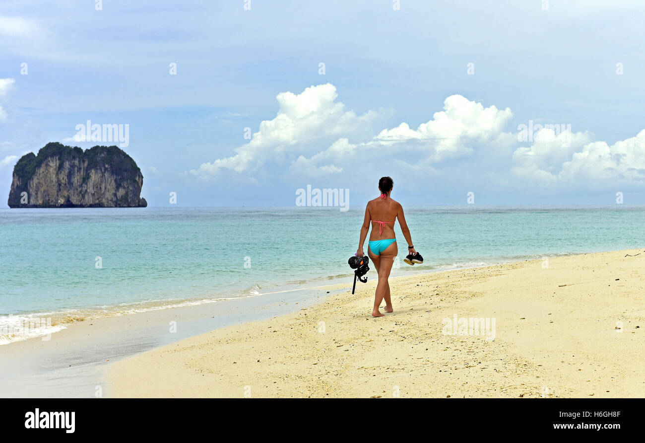 Rivestito di Bikini donna cammina lungo una spiaggia di Isola in Thailandia, portante un set snorkel Foto Stock
