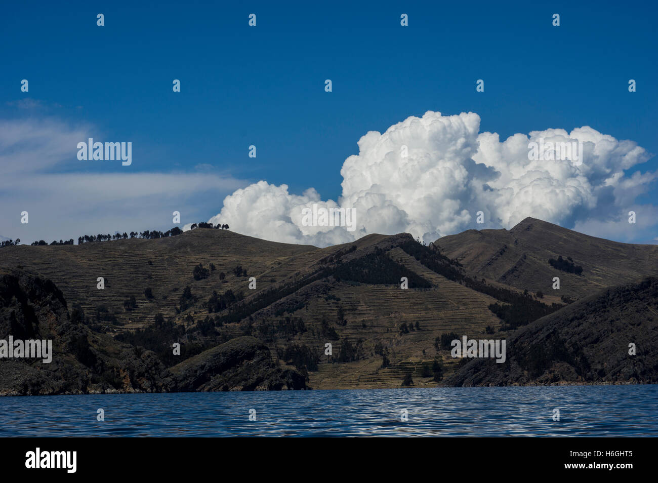 Colpisce il bianco delle nuvole sopra una collina con alberi contro un cielo blu del lago Titicaca, Bolivia. Il lago di frontiere anche il Perù. Foto Stock