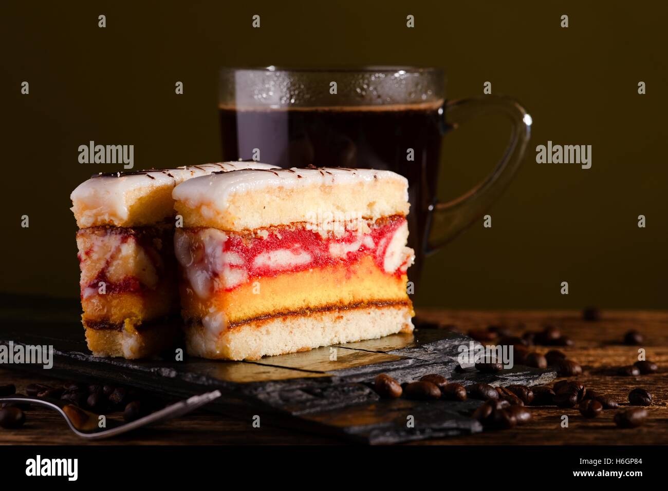 La foto in orizzontale dei due fette di dolce deserto con gli strati di colore per lo zucchero sulla sommità poste sul pezzo di pietra nera. Tazza di coff Foto Stock