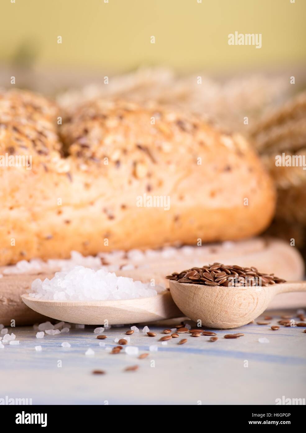 Foto verticale con vista sul blu chiaro pannello di legno con la pagnotta di pane cereali, alcune spighe di grano e due cucchiai di sale e flusso Foto Stock