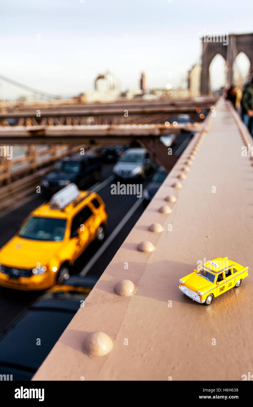 Modello di un classico giallo taxi su una trave in acciaio sul ponte di Brooklyn, con un vero e proprio taxi passando sul livello inferiore strada asfaltata. Foto Stock