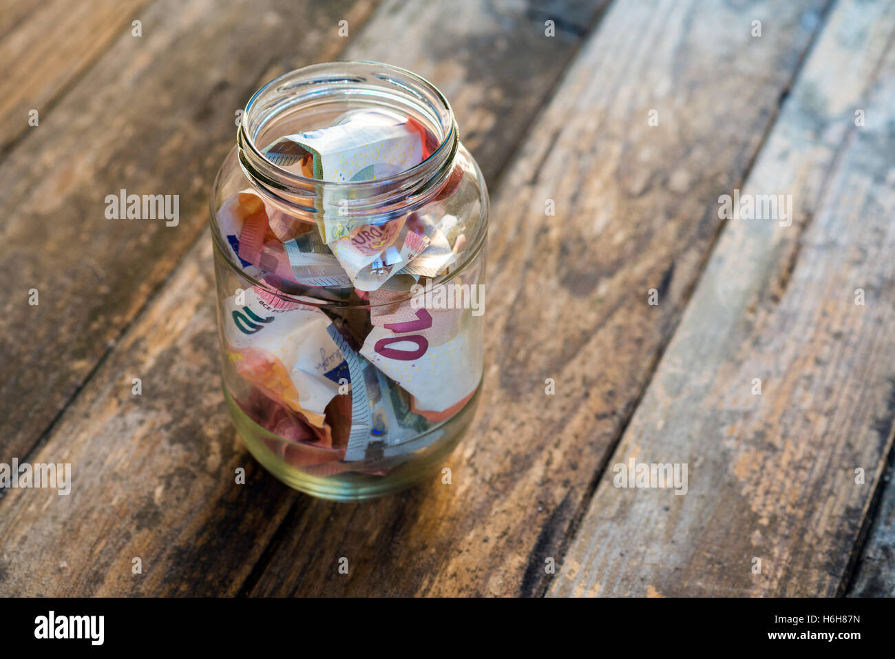 Il denaro in un barattolo di vetro sul tavolo di legno Foto Stock