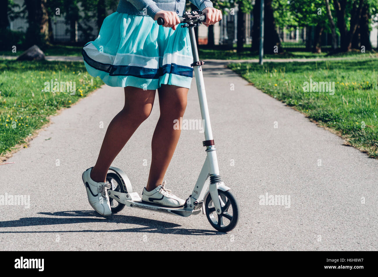Le gambe della giovane donna in abiti sul kick scooter. Tonica Instagram retrò effetto vintage Foto Stock