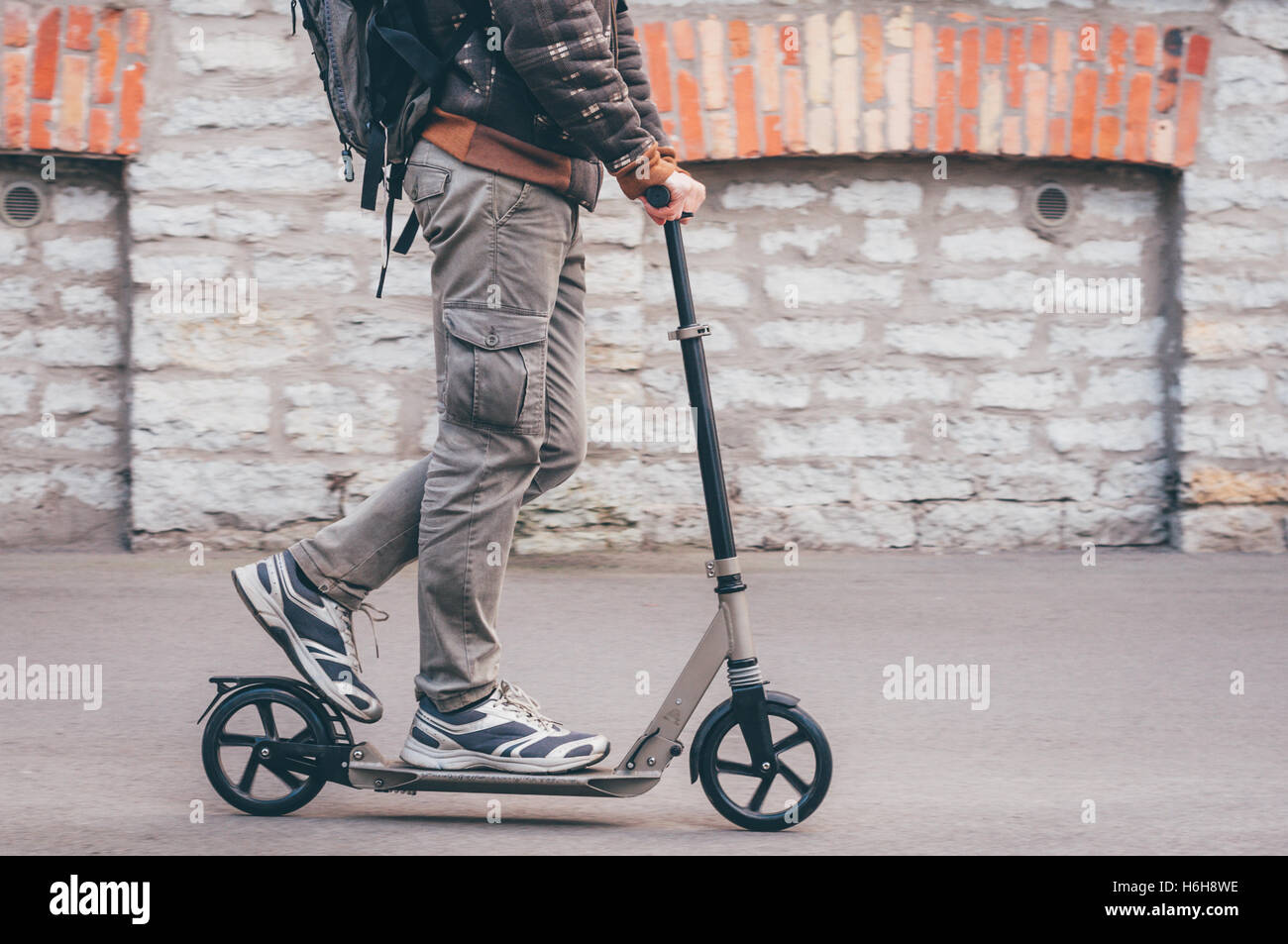 Giovane uomo in abbigliamento casual su kick scooter sulla strada della citta'. Tonica Instagram retrò effetto vintage Foto Stock