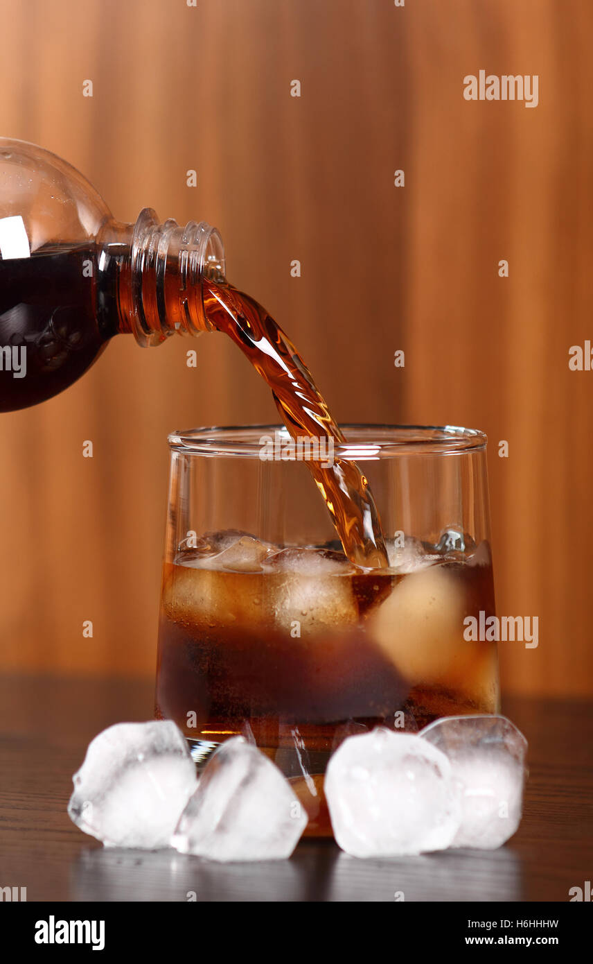 Versando cola dalla bottiglia di plastica nelle rocce di vetro con cubetti di ghiaccio Foto Stock