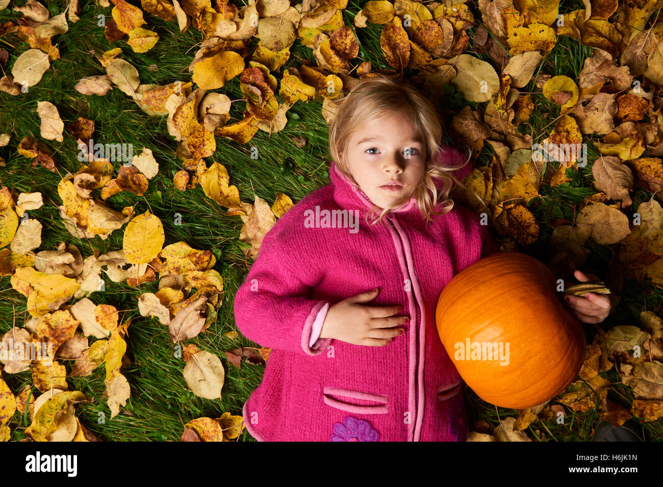 Bambino carina ragazza bionda giacente in foglie di autunno con la zucca. Foto Stock