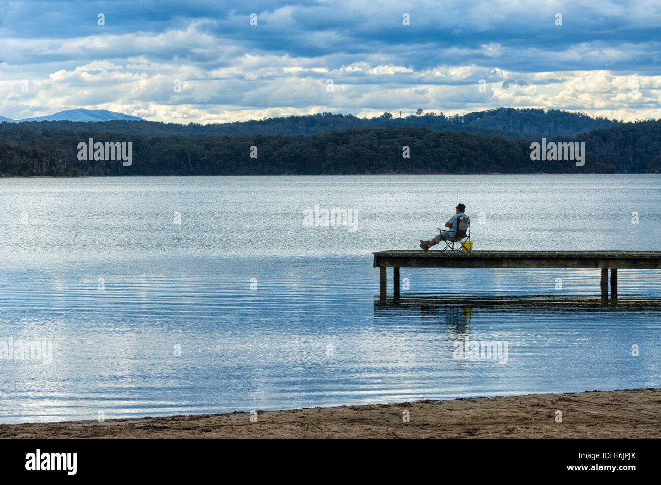Pescatore seduto sul molo al Lago Wallaga la sera, vicino Bermagui, Nuovo Galles del Sud, Australia Foto Stock
