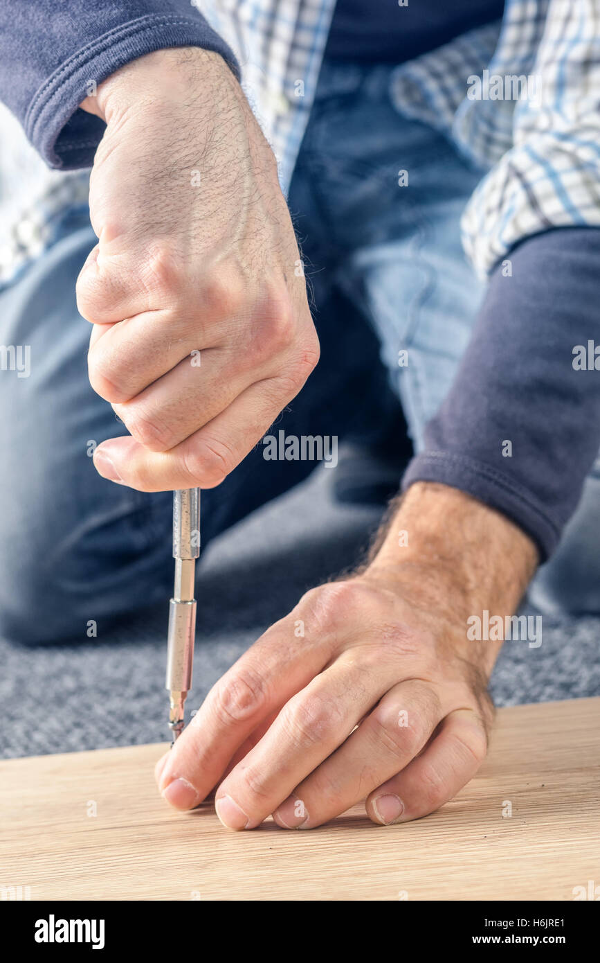 L'uomo assemblaggio di mobili a casa sul pavimento, a mano con un cacciavite Foto Stock