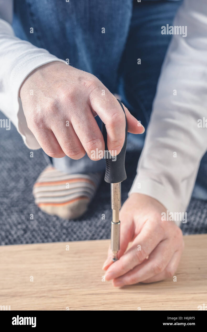 Donna di assemblaggio di mobili a casa sul pavimento, a mano con un cacciavite Foto Stock